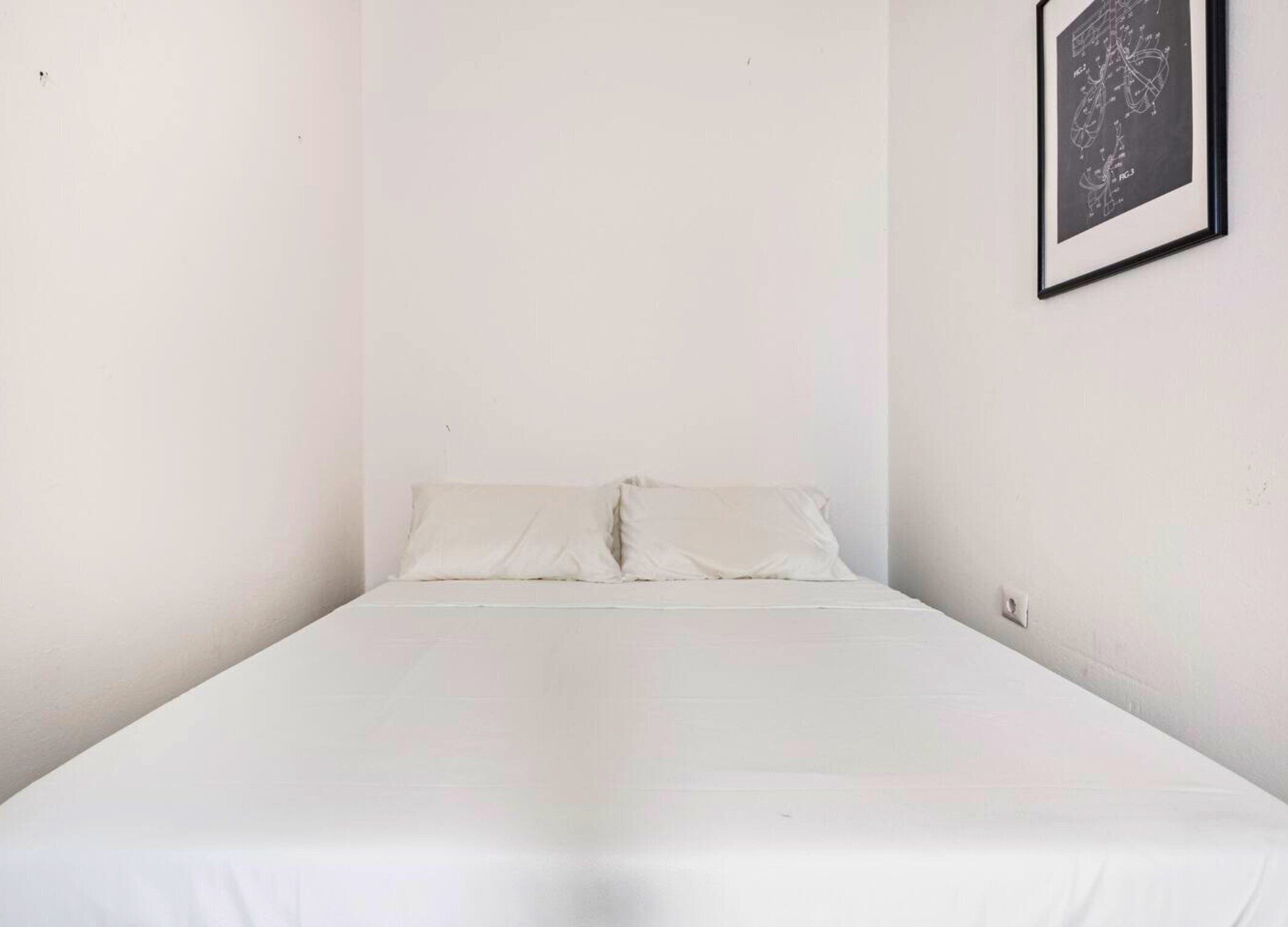 Ein Einzelbett mit weißer Bettwäsche in einem Raum mit schlichten weißen Wänden.