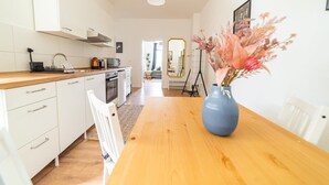 Una cocina moderna con armarios blancos, encimera de madera y un florero azul con flores sobre una mesa de comedor.