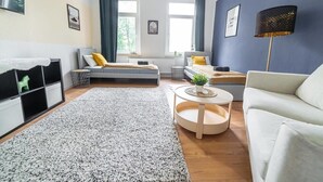 Una sala de estar moderna con sofá, una mesita redonda, una cama con cabecera y una ventana con cortinas.