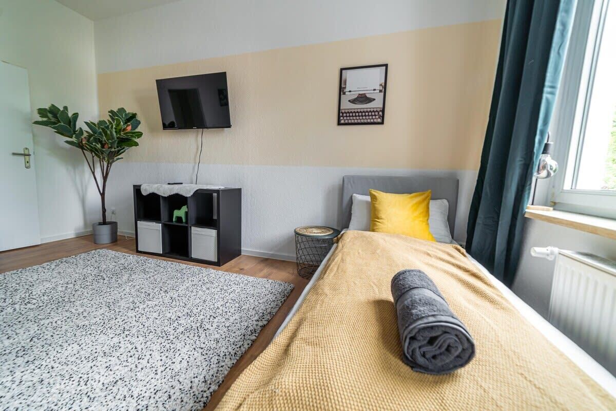 Ein modernes Hotelzimmer mit einem Bett, einem Fernseher, einer kleinen Pflanze und einem Fenster mit Vorhängen.