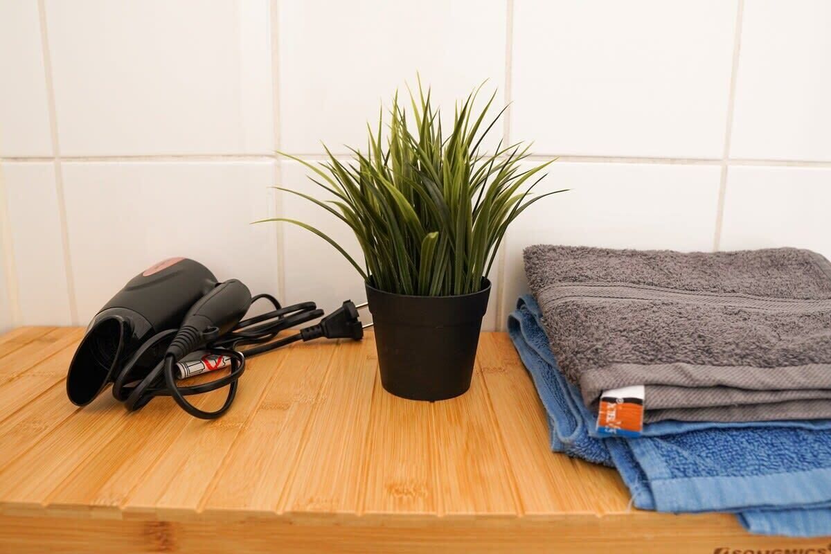 Een badkamer met een houten aanrecht, een zwarte haardroger, een potplant en opgevouwen handdoeken.
