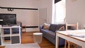 A modern living room with a flat-screen TV, a sofa, a coffee table, and a dining table. - FullHouse | Halle | T28 Panda Apt. (Halle (Saale))