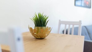 Um pequeno pote redondo dourado com padrão floral contendo plantas verdes sobre uma mesa de madeira.
