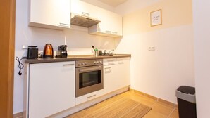 Uma cozinha compacta com armários brancos, fogão, forno e cafeteira.