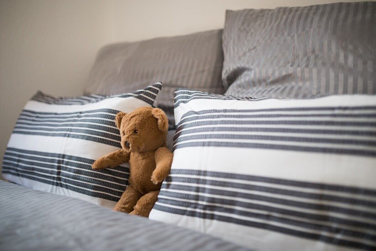 A bed with striped bedding and a teddy bear.