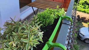 Un balcone con un tavolo di legno, una fioriera verde con diverse piante e una rete di sicurezza rossa.