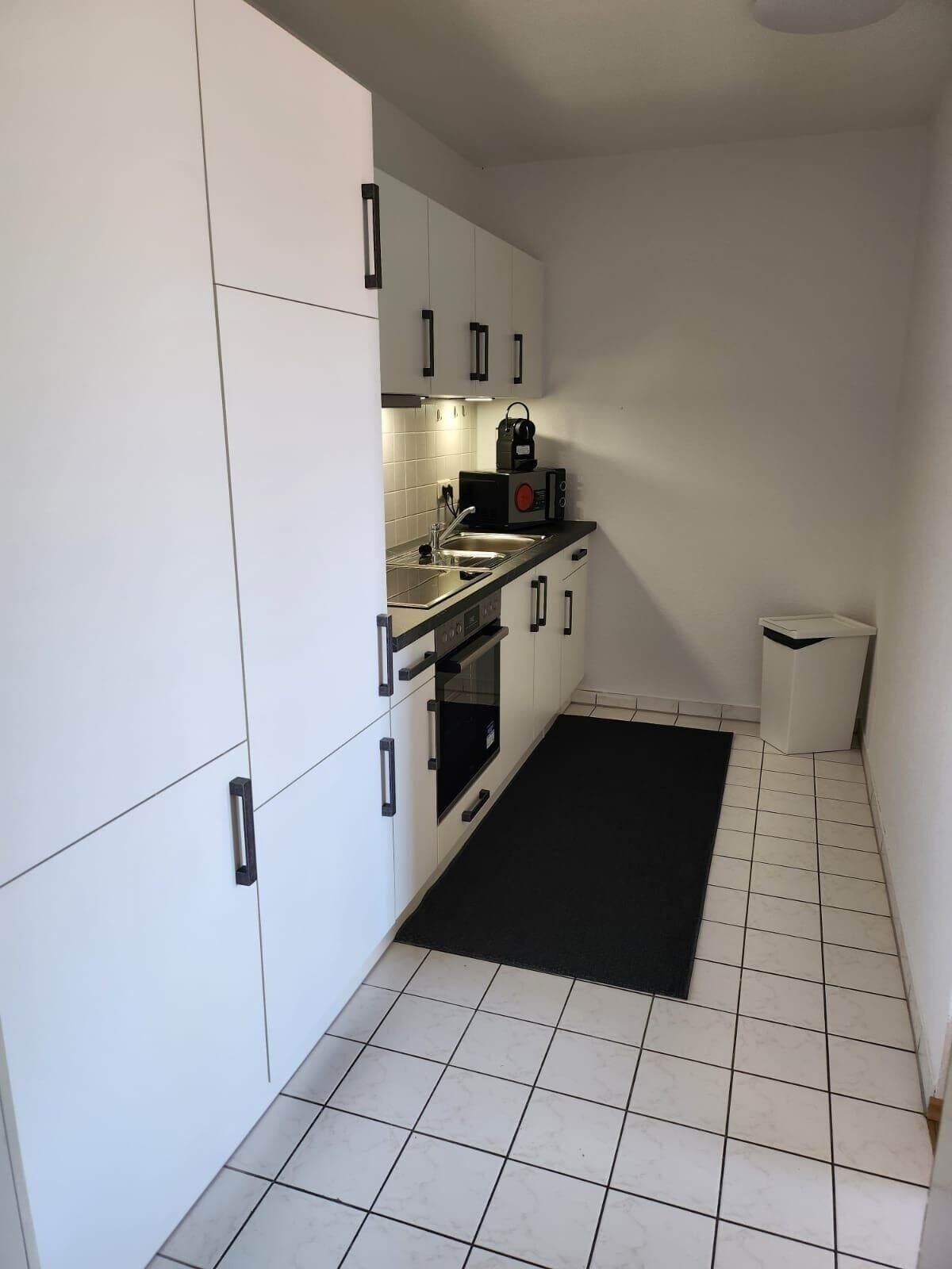 A compact kitchen with white cabinets, a black countertop, and a tiled floor.