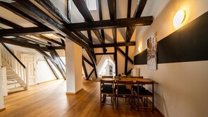 Une pièce spacieuse avec des poutres apparentes, un coin repas avec une table et des chaises, et un escalier menant à un autre niveau.