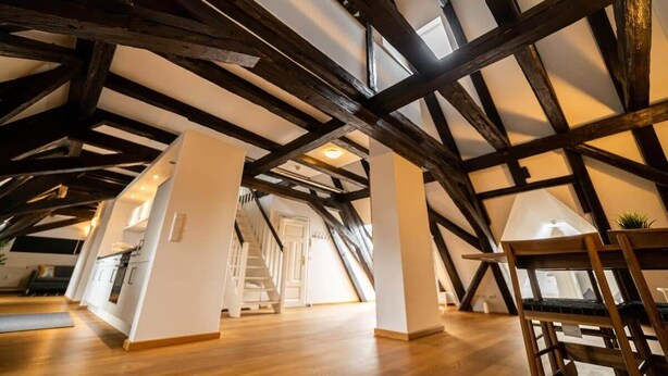 Une chambre mansardée avec des poutres apparentes, un plancher en bois et un escalier menant à un autre niveau.