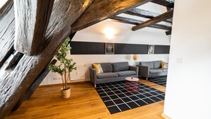 Une chambre mansardée avec des poutres apparentes, un canapé gris, une petite table ronde et un tapis à motifs noir et blanc.