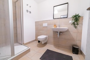 Ein modernes Badezimmer mit einer Duschkabine aus Glas, einer weißen Toilette, einem Waschbecken mit Spiegel und einer Topfpflanze.