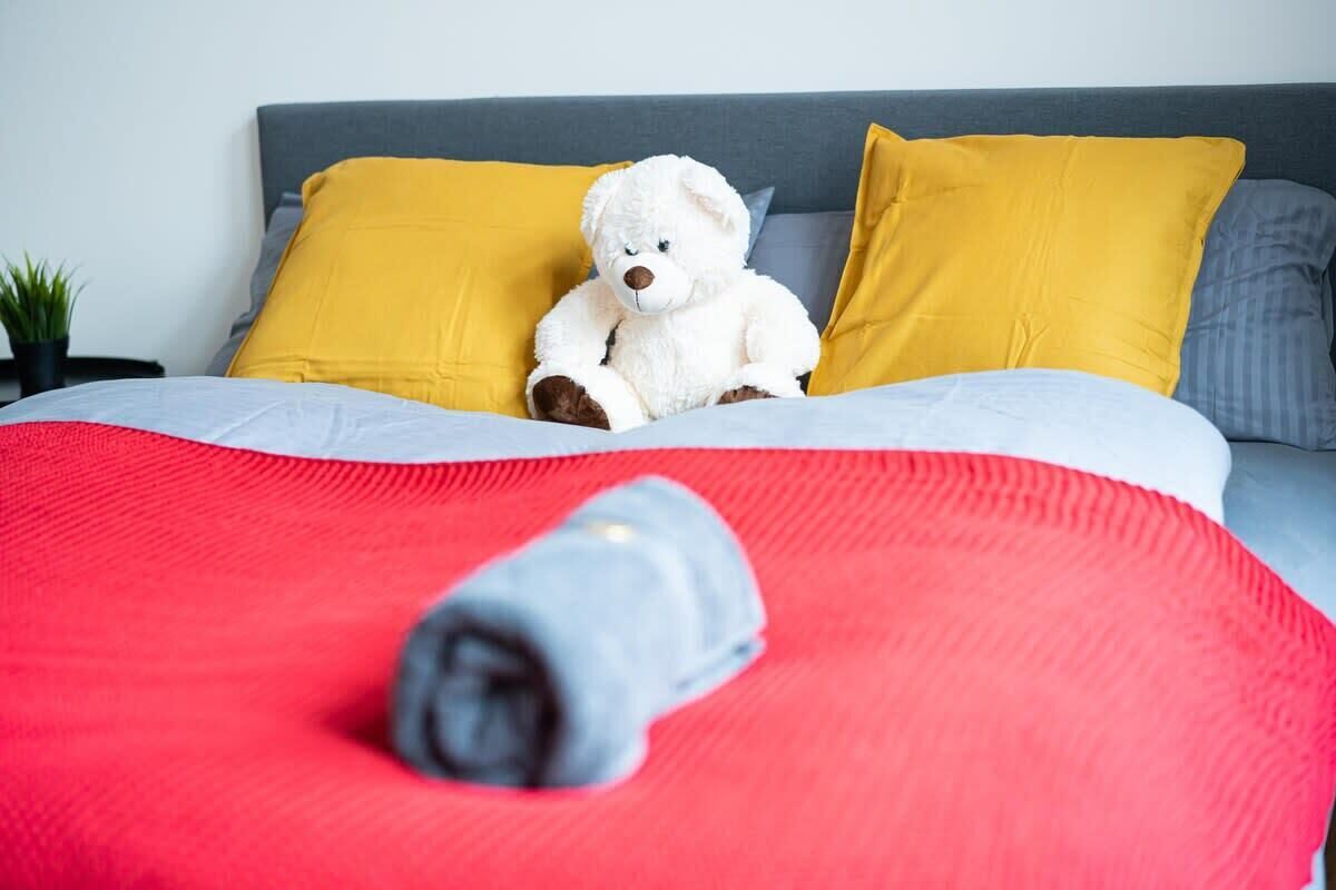 A bed with a white teddy bear, two yellow pillows, and a red blanket.