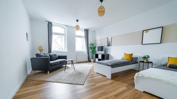 A modern, well-lit living room with a sofa, a bed, and a TV. - FullHouse | Magdeburg | L10-2 | FamilienApartment (Magdeburg)