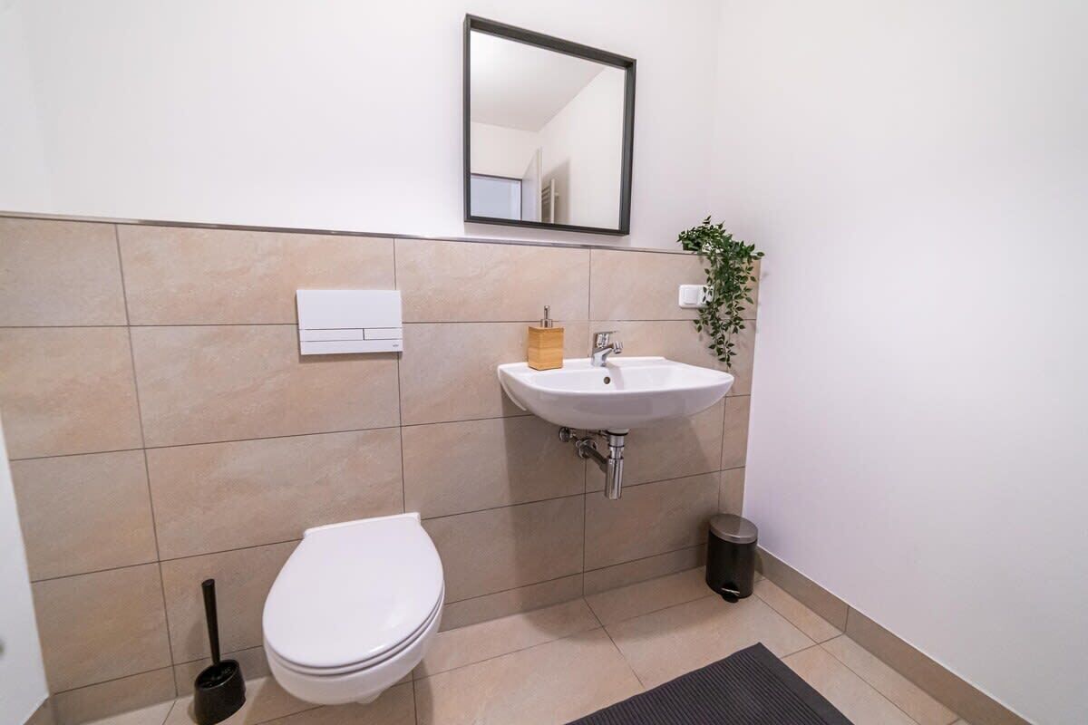 A bathroom with a white toilet, a sink with a mirror above it, and a trash bin.