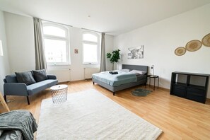 Un dormitorio moderno con cama, un sofá gris, una mesita auxiliar y un ventanal grande.