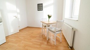 A small, bright room with a wooden floor, a white radiator, a window, and a table with two chairs.
