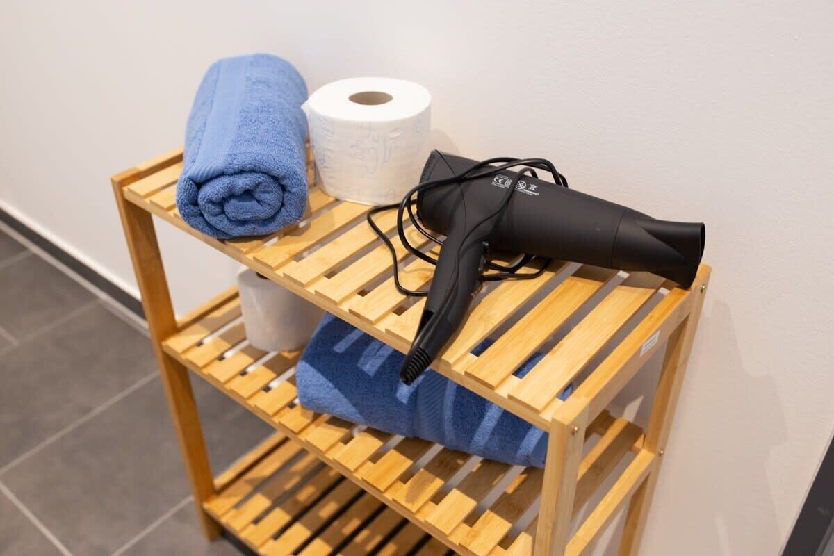 A wooden shelf with a blue towel, a roll of toilet paper, and a black hairdryer.