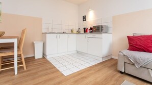 Eine moderne Küche mit weißen Schränken, einem Esstisch mit Stühlen und einer Couch mit roten Kissen.