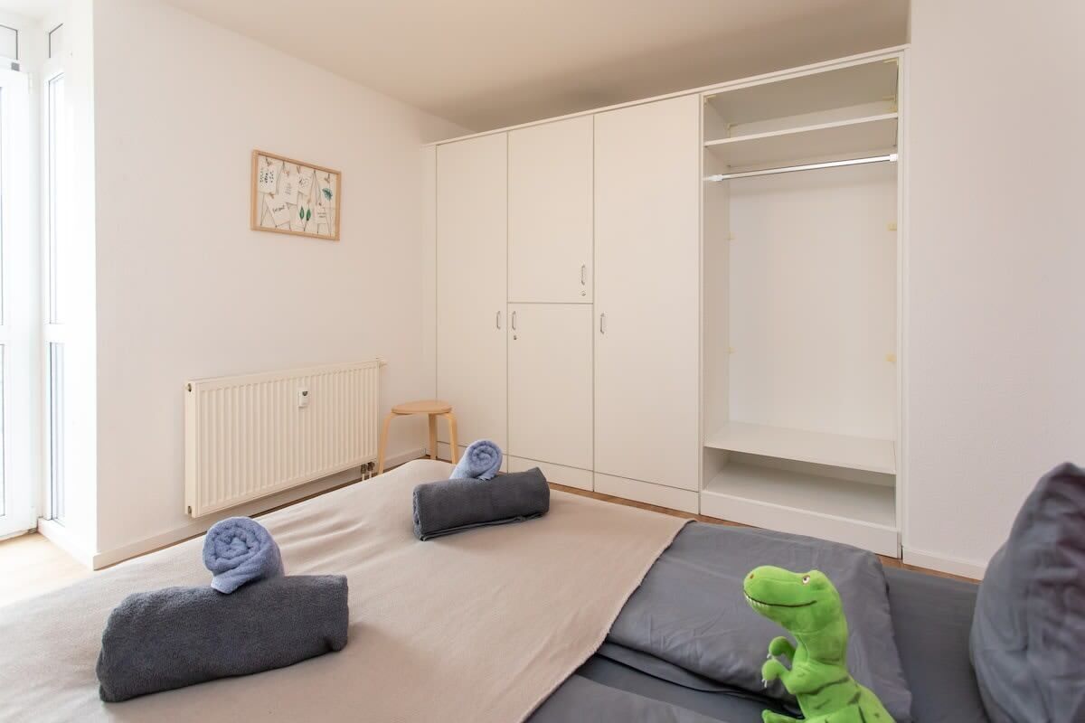 Ein Schlafzimmer mit Bett, Kleiderschrank, Heizkörper und einem kleinen Hocker.