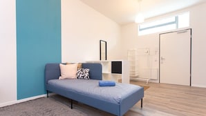 Une chambre moderne avec un canapé bleu, une petite commode blanche, un tapis gris et un plancher en bois.
