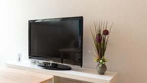 Un téléviseur à écran plat posé sur un meuble blanc, avec un petit vase de fleurs à côté.
