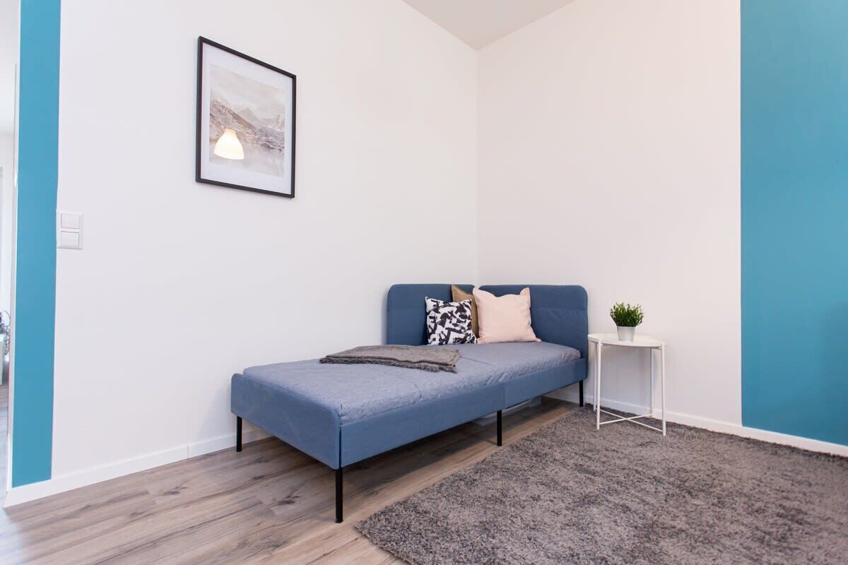 A small, modern room with a blue sofa, a small side table with a plant, and a framed picture on the wall.