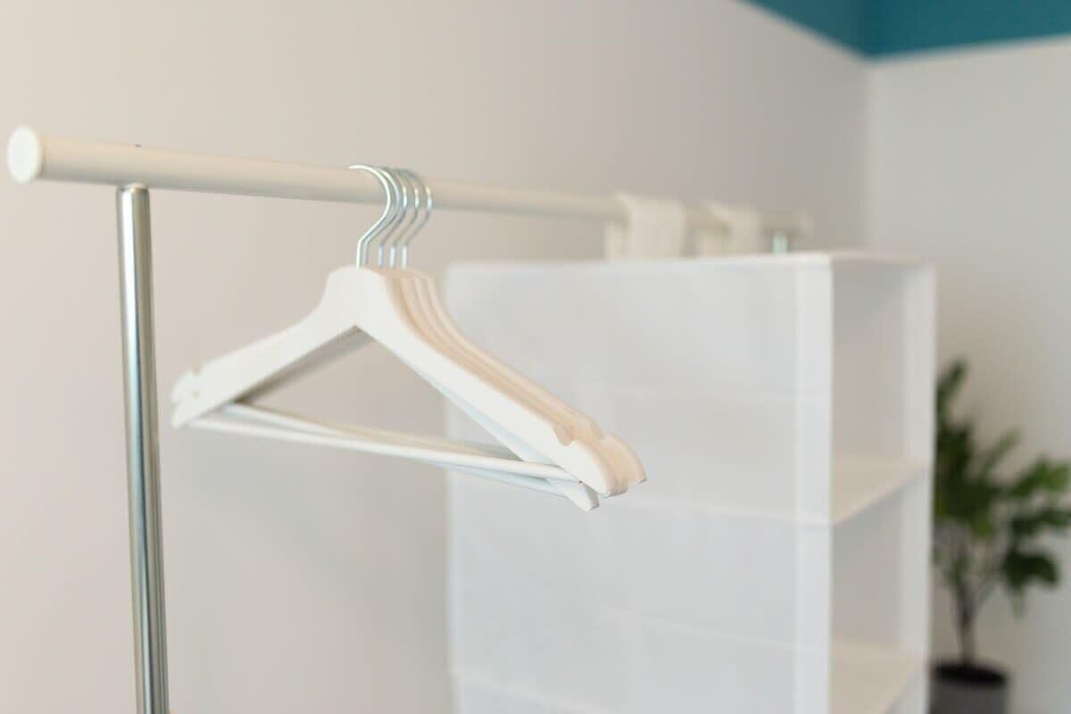 Une étagère en métal blanc avec un porte-vêtements en bois, dans une salle de bain aux murs blancs et au plafond bleu.