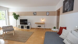 Een moderne woonkamer met een bank, een televisie, een bureau en een plant.