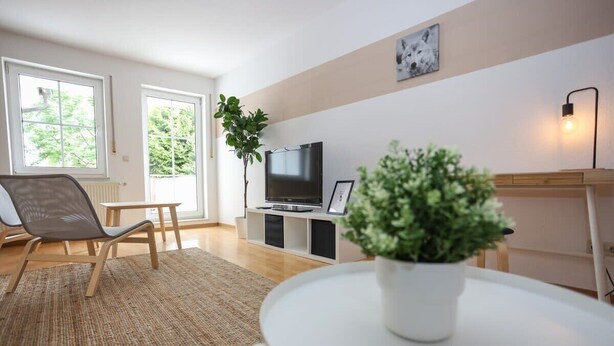 Een moderne woonkamer met een flatscreen televisie, een potplant en een eettafel.