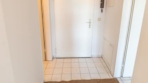 Ein Flur mit einer weißen Tür, einer Pendelleuchte und einem braunen Teppich.