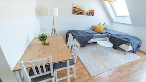 Ein gemütlicher Raum mit einem Holztisch, weißen Stühlen, einem kleinen Topfpflanz und einem Bett mit grauer Decke, einem runden weißen Beistelltisch und einem großen Fenster mit Landschaftsblick.