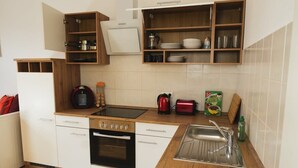 Een kleine keuken met witte kastjes, een inbouwoven, een magnetron, een broodrooster en een spoelbak.