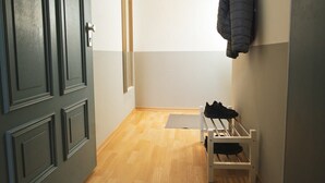 Een hal met een houten vloer, een kapstok met een jas en een deur met een deurklink.