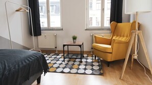 Een hotelkamer met een bed, een gele fauteuil, een tafeltje met een plant en een lamp.
