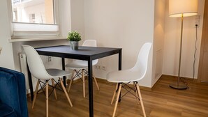 Un coin repas avec une table noire, quatre chaises blanches, une petite plante en pot et une lampe sur pied.