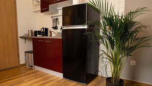 Une cuisine de taille réduite avec un réfrigérateur noir, un plancher en bois et une plante en pot.