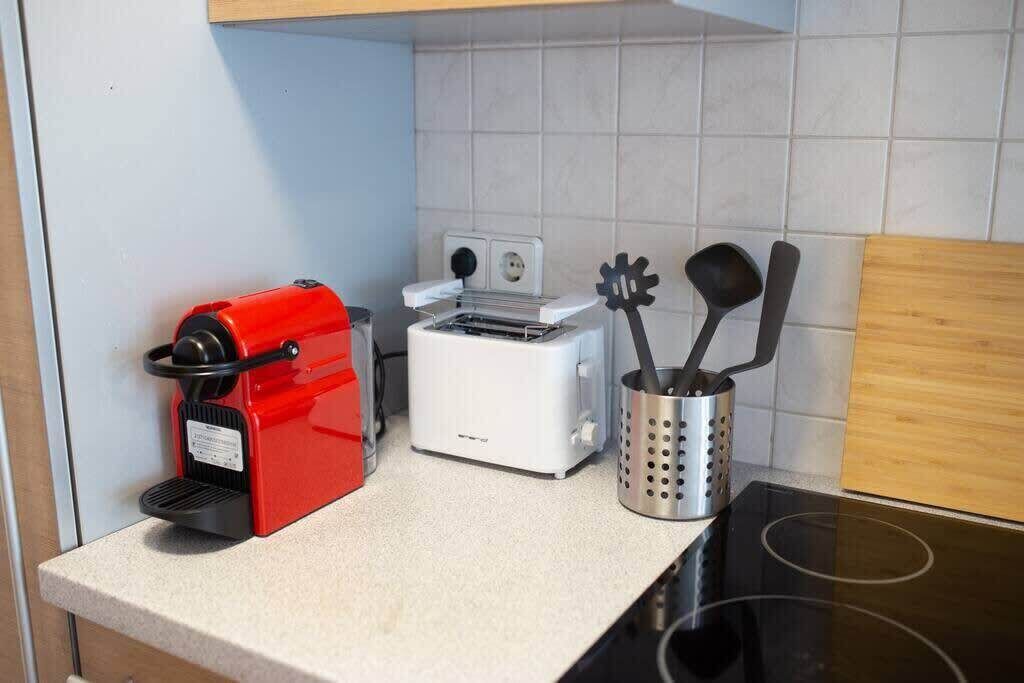 Une cuisine avec une machine à café rouge, un grille-pain blanc et un porte-ustensiles en métal sur le comptoir.