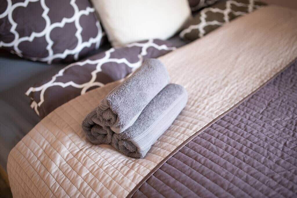 Un lit bien fait, avec des serviettes pliées, une couvre-lit matelassée et des coussins à motifs.