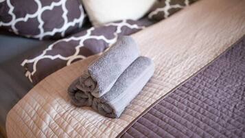 Un lit bien fait, avec des serviettes pliées, une couvre-lit matelassée et des coussins à motifs.