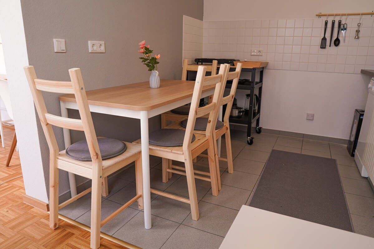 A dining area with a wooden table and chairs, a vase with flowers, and kitchen utensils on the wall.