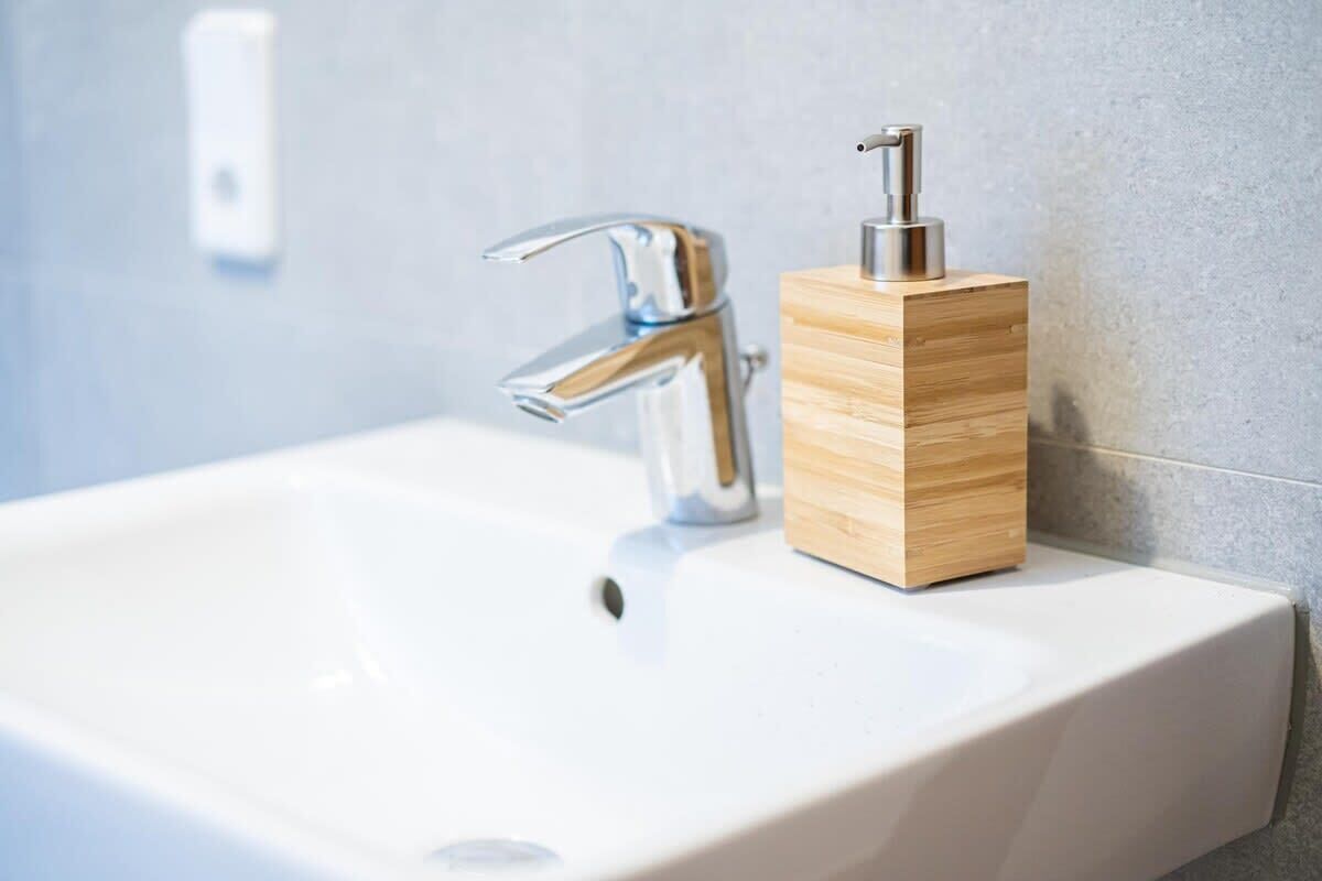 Un lavamanos moderno con grifo cromado y dispensador de jabón de madera.