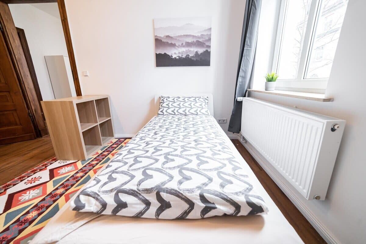 A bedroom with a bed, a radiator, a window with a plant, and a painting on the wall.