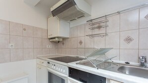 Cucina con mobili bianchi, un fornello, un forno, un lavello e una cappa aspirante a soffitto.