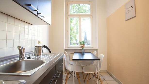 Une cuisine équipée d’un évier, d’une cuisinière et de chaises blanches disposées autour d’une table.