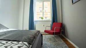 Une chambre à coucher avec un lit, une chaise rouge, une fenêtre avec des rideaux bleus et un radiateur.