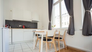 Eine moderne Küche mit weißen Schränken, einer schwarzen Arbeitsplatte und einem Fischgrätparkettboden. Es gibt zwei weiße Stühle mit schwarzen Kissen und einen weißen Tisch.