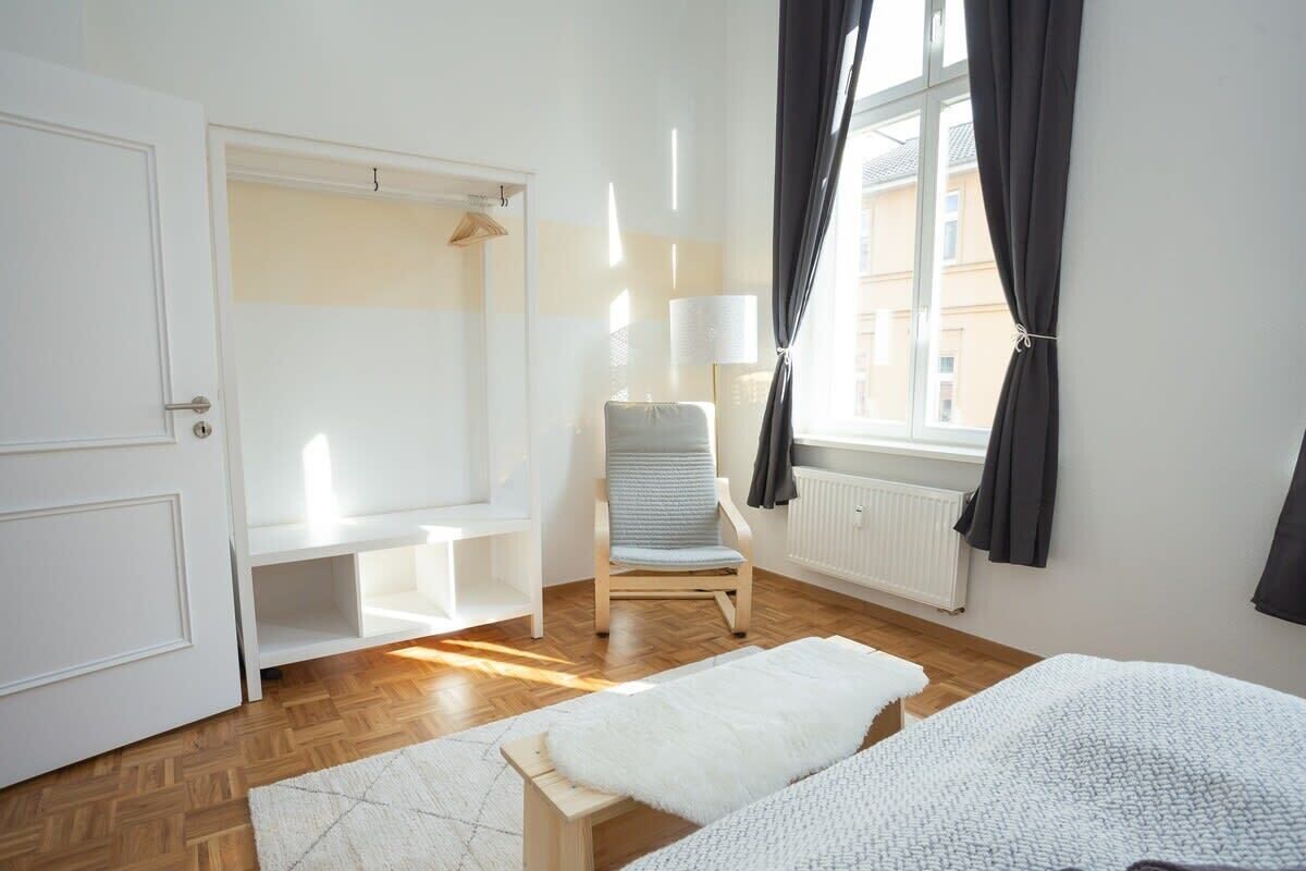 Ein Schlafzimmer mit Bett, Stuhl, Kleiderschrank und einem Fenster mit Vorhängen.