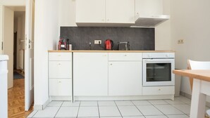 Eine kleine Küche mit weißen Schränken, einer schwarzen Arbeitsplatte, einem roten Wasserkocher und einem weißen Backofen.