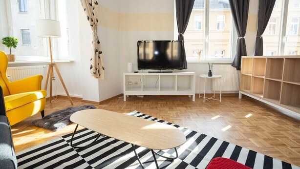 Ein modernes Wohnzimmer mit einer Couch, einem Fernseher, einer Lampe und einem Streifen Teppich.