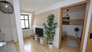 Ein modernes Wohnzimmer mit einem Flachbildfernseher, einer großen Kübelpflanze mit Bambus, Holzboden und einer Schiebetür zu einem anderen Raum.